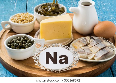 Products Containing Sodium (seaweed, Salted Herring, Capers, Pine Nuts, Soy Sauce, Egg) On A Round Cutting Board And A Blue Wooden Background