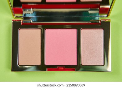 Products For Contouring Face. Palette With Blush Bronzer And Highlighter On A Green Background