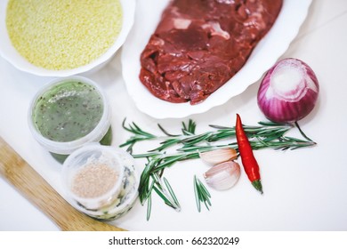 Products for cooking dinner on a white table: meat, couscous, chili, onion, garlic, rosemary