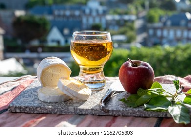 Products of Normandy, cow neufchatel lait cru cheese and glass of apple cider drink with view on houses of Etretat village on background, Normandy, France - Shutterstock ID 2162705303