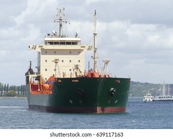 Products Tanker Ship Maneuvering In The Harbor With Coastline And Cloudy Sky In Background. Horizontal  Three-quarter Front View.