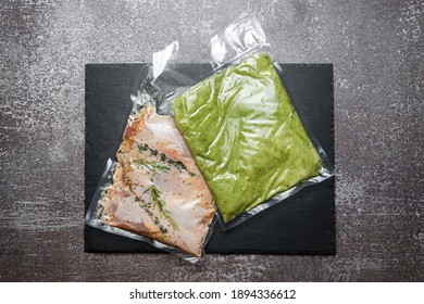 Products In Vacuum Packaging On Black Slate Board. Chicken Meat With Herbs And Green Beans Puree, Vacuum Sealed Food Ready For Sous Vide Cooking. Sous-vide, New Technology Cuisine In Quarantine Time.