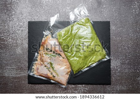 Products in vacuum packaging on black slate board. Chicken meat with herbs and green beans puree, vacuum sealed food ready for sous vide cooking. Sous-vide, new technology cuisine in quarantine time.
