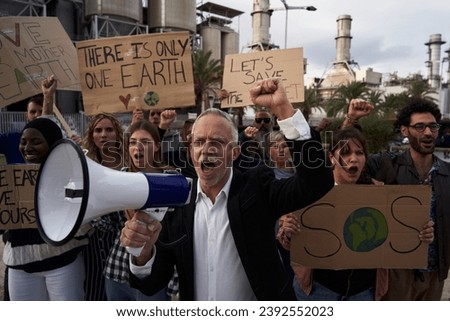 Pro-earth demonstration with banners for climate change. Mature man with megaphone in a protest against pollution. Group of diverse people outdoors manifesting for global warming.