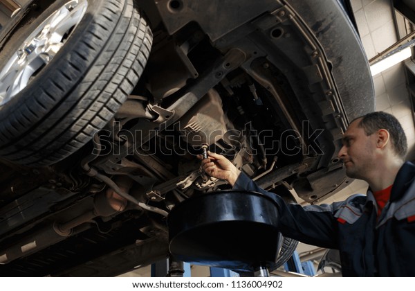 Profecional car\
mechanic changing motor oil in automobile engine at maintenance\
repair service station in a car\
workshop.