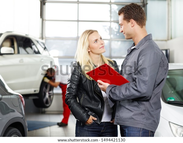 a profeesional employee of the tire and car service\
workshop have a sale talk with a blonde female customer and the\
mechanical emplpyee in the red overall make some repairs at the car\
in the back