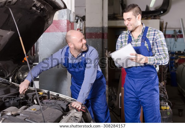 Professinal car mechanic in an automotive\
repair shop helps insurance agent to calculate\
loss