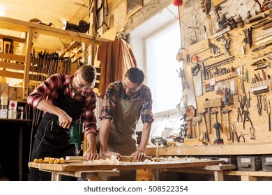 profession, carpentry, woodwork and people concept - two carpenters with electric drill drilling wood plank at workshop - Powered by Shutterstock