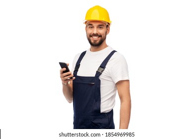 profession, construction and building - happy smiling male worker or builder in yellow helmet and overall with smartphone over white background