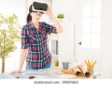 Profession And Job Occupation Concept. Young Asian Architect Woman Experience Test VR Virtual Reality Glasses Technology To Simulation New Design While At The Desk In Creative Office Studio.