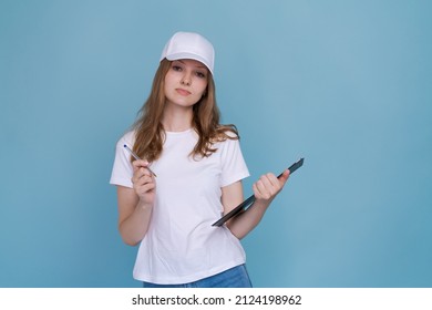 Profession, job and people concept - happy smiling delivery woman in white uniform with document holding pen on blue background. Caucasian girl promoter in white football and cap
