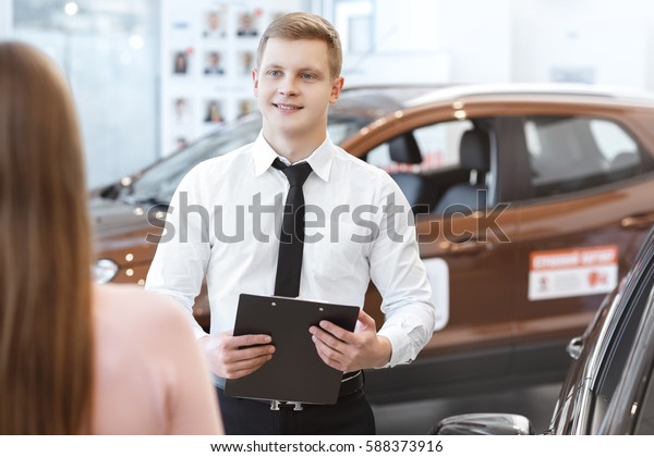 Professional advice. Rearview shot of a female\
client buying a new car at the dealership talking to the salesman\
handsome car dealer smiling while helping his female client\
profession experience\
trust