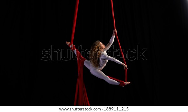 Professional aerialist circus\
performer on red bright aerial silks performs balance on a\
splits