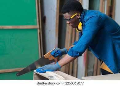 Professional African American male carpenter cutting lumber wood with handsaw in the wood workshop. Male carpenter working at the furniture workshop - Powered by Shutterstock