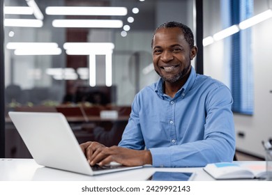 Professional African American male entrepreneur with a beaming smile at his office desk using a laptop. - Powered by Shutterstock