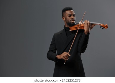 Professional African American male violinist in elegant black suit performing solo on gray background - Powered by Shutterstock