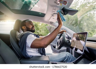 Professional African Man, Car Owner Or Service Worker, Cleaning Car Interior, Car Mirror Using Microfiber Clothes. Car Detailing. Modern Futuristic Vehicle With Touchscreen Display. Selective Focus