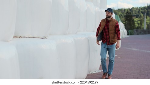 Professional agronomist walking hay stack on season countryside. Agribusiness owner check bales pile at autumn farmland. Modern organic agribusiness.