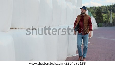 Professional agronomist walking hay stack on season countryside. Agribusiness owner check bales pile at autumn farmland. Modern organic agribusiness.