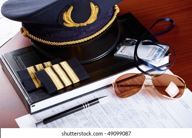 Professional Airline Pilot Hat And Id Holder With Epaulets And Sun Glasses Laying On Log Book And Flight Plan.