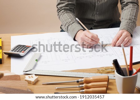 Professional architect and construction engineer working at office desk hands close-up, he is drawing on a building project with a pencil and a ruler
