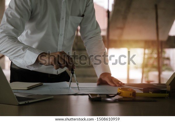professional architect, engineer or interior\
hands drawing with divider compass and blueprint on workplace desk\
in office center at construction site, construction, engineering\
and business\
concept