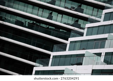 A professional architectural shot capturing the rhythmic, staggered design of a modern apartment complex. The image emphasizes the clean lines of white structural panels and the reflective surfaces of glass balconies from a dynamic angle.