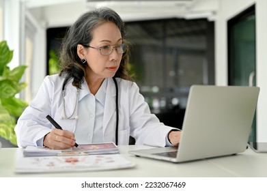 Professional Asian aged female doctor specialist working at her desk, using laptop computer, research medical paper on the internet. - Powered by Shutterstock