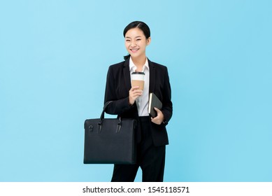 Professional Asian businesswoman in formal suit holding briefcase coffee cup and book isolated on light blue background - Powered by Shutterstock