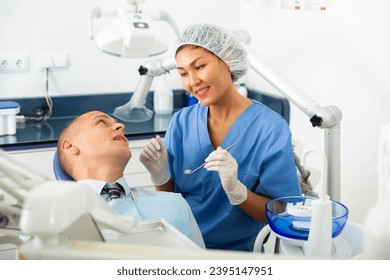 Professional asian female dentist examining male patient teeth with dental tools - mirror and probe - Shutterstock ID 2395147951