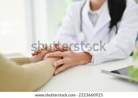 Professional Asian female doctor touching her patient hands to make her patient feel relaxed and reassured. close-up and cropped image