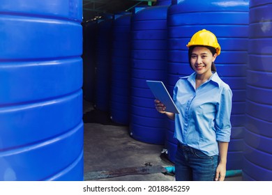 Professional Asian Female Engineer Wearing A Helmet Uses A Laptop To Inspect A 2,000 Liter Tank Of Clean Water In A Standard Storage Area At A Processed Drinking Water Factory.