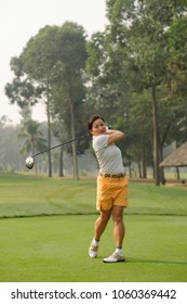 Professional Asian Golfer Wearing T-shirt And Shorts Teeing Off Ball While Having Training At Golf Course, Full Length Portrait