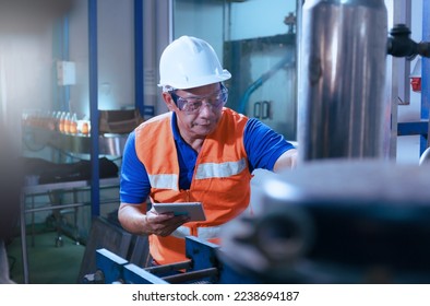 Professional Asian male engineer in helmet using the tablet to work, inspect and maintain electrical cabinet. Machines in a beverage factory, beverage industry concepts expert worker - Powered by Shutterstock