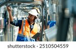 Professional Asian man engineer in safety uniform working on digital tablet at outdoor construction site rooftop. Industrial technician worker maintenance checking building exterior air HVAC systems.