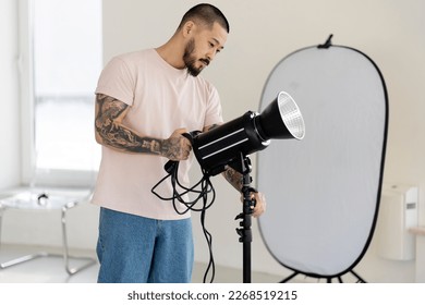 Professional Asian photographer adjusts lamp with lighting, preparing for shooting.  A young man works in a professional photo studio  - Powered by Shutterstock