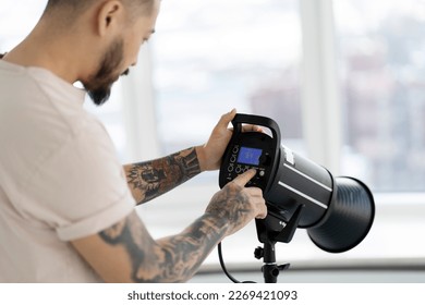 Professional asian photographer with stylish tattoos setting up lighting in modern studio. Assistant preparing equipment for photo shoot, selective focus  - Powered by Shutterstock