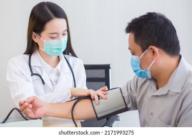 Professional Asian Woman Doctor Uses A Blood Pressure Meter With A Man Patient To Check His Health At Hospital. They Wear A Medical Face Mask To Protect Respiration System Infection.