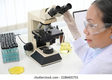 A Professional Asian-aged Female Scientist Or Medical Chemist Supervisor Examining A Virus Specimen With A Microscope In The Lab. Close-up Image