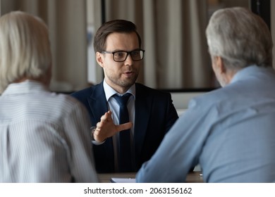 Professional Assistant. Confident Young Man Financial Advisor Real Estate Agent Talking Consulting Retired Couple. Experienced Businessman Manager Lawyer Help Clients Aged Spouses On Meeting At Office