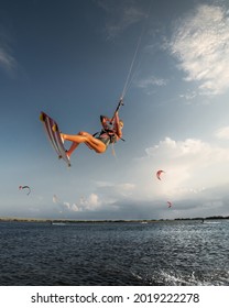 Professional athlete kitesurfer young caucasian woman doing a trick in the air against the backdrop of the sunset sky and clouds. Professional kitesurfing and kite culture training