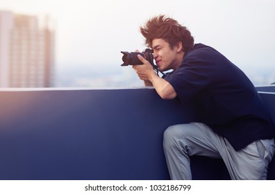 Professional attitude. Young male paparazzi photographer making photos while standing on the rooftop - Powered by Shutterstock