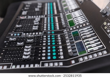 The professional audio mixing console features numerous sliders and controls, indicating a live sound setup with various channels active and ready for adjustments.