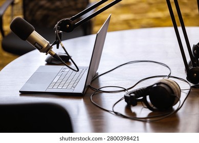 Professional audio recording setup for broadcasting and content creation with a microphone, laptop, and headphones arranged on a polished wooden surface