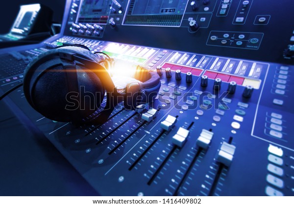 Professional audio studio\
sound mixer console board panel with recording , faders and\
adjusting knobs,TV equipment. Blue tone and close-up image with\
flare light\
effect.