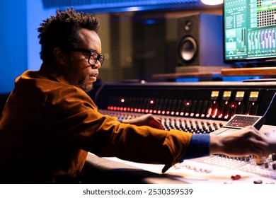 Professional audio technician recording and editing songs by adjusting volume levels with switchers. Music producer creating tracks with mixing console and software in post production studio. - Powered by Shutterstock