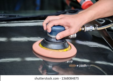 Professional Auto Detailer Hand Holding Air Random Orbital Sander Or Dual Action Polisher While Waxing Paint Surface Of Shiny Carbon Kevlar Hood. Car Detailing, Car Wash, And Paint Sealant Concept