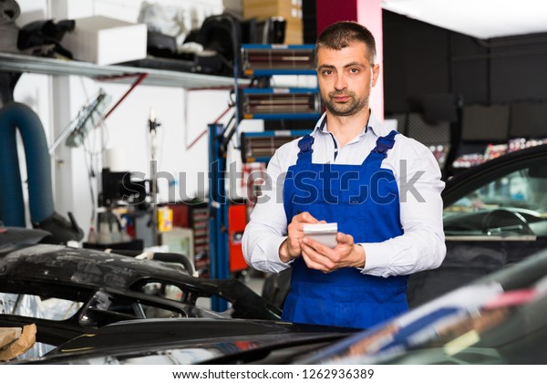 Professional auto mechanic recording list of\
works on car repair in auto workshop\
