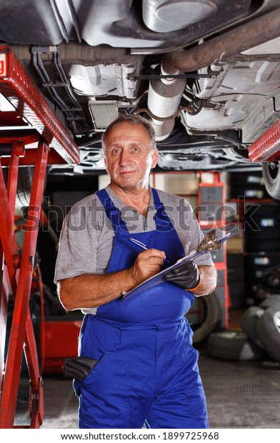 Professional auto mechanic recording list of\
works on car repair in auto workshop\
..