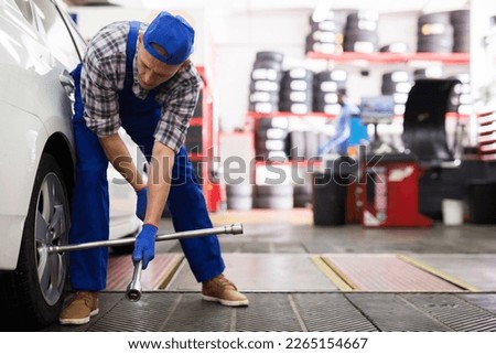 Professional auto mechanic screwing the wheel with a wrench in workshop